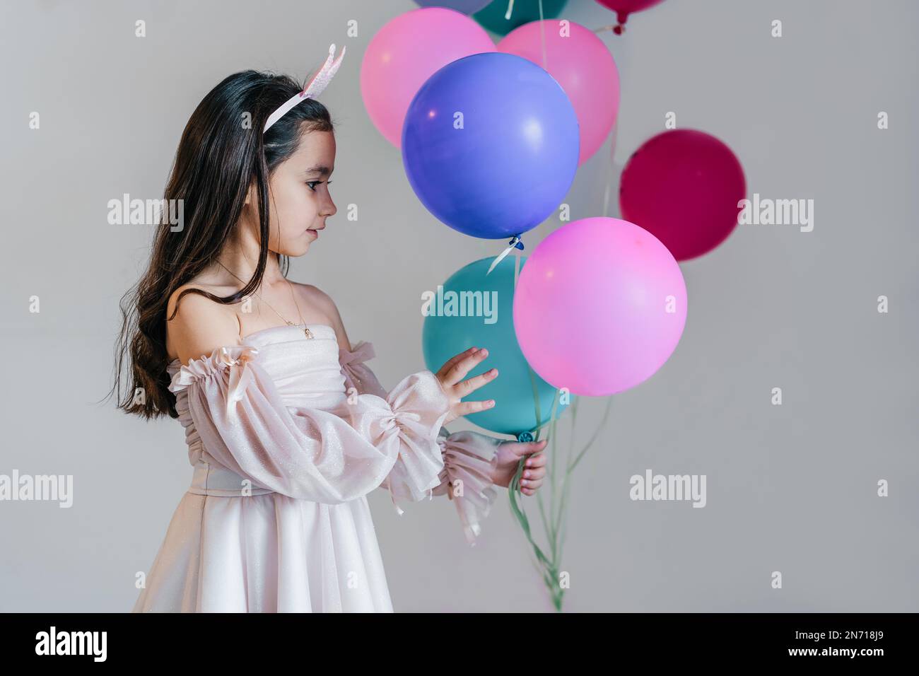 Hübsches, kleines brünettes Mädchen in einem pinkfarbenen Kleid und einer Krone mit blauen, grünen und pinken Ballons. Stockfoto