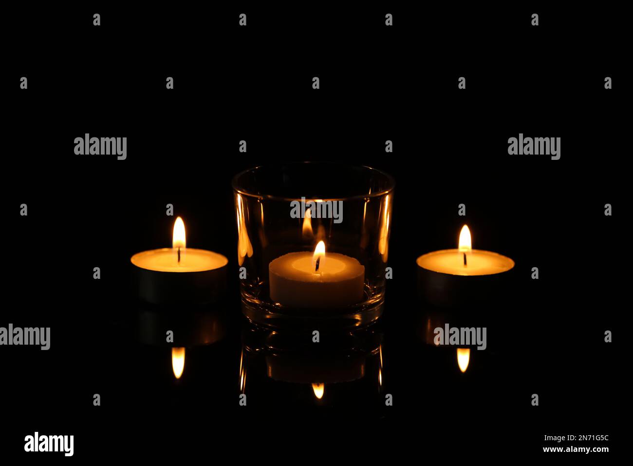 Kleine Wachskerzen brennen in der Dunkelheit. Bestattungssymbol Stockfoto