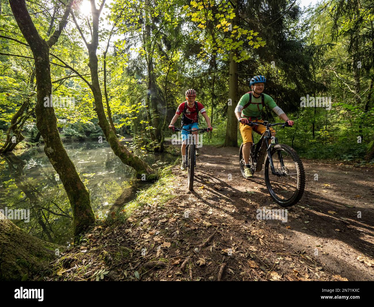 E-Mountain-Biker am Fuße des „Hunnerbuer“, einer Sandsteinformation, wo einige Quellen sofort gefangen werden und die Pools füttern. Der Hunnerbuer gehört zu den Sandsteinfelsen, die das ganze Land von Ost nach West durchqueren (einschließlich der Stadt Luxemburg). Der gesamte felsige Bereich ist auch ein wichtiger Frühlingsbereich. Viele Quellen werden gesammelt und versorgen das Trinkwassernetz Luxemburgs. Stockfoto