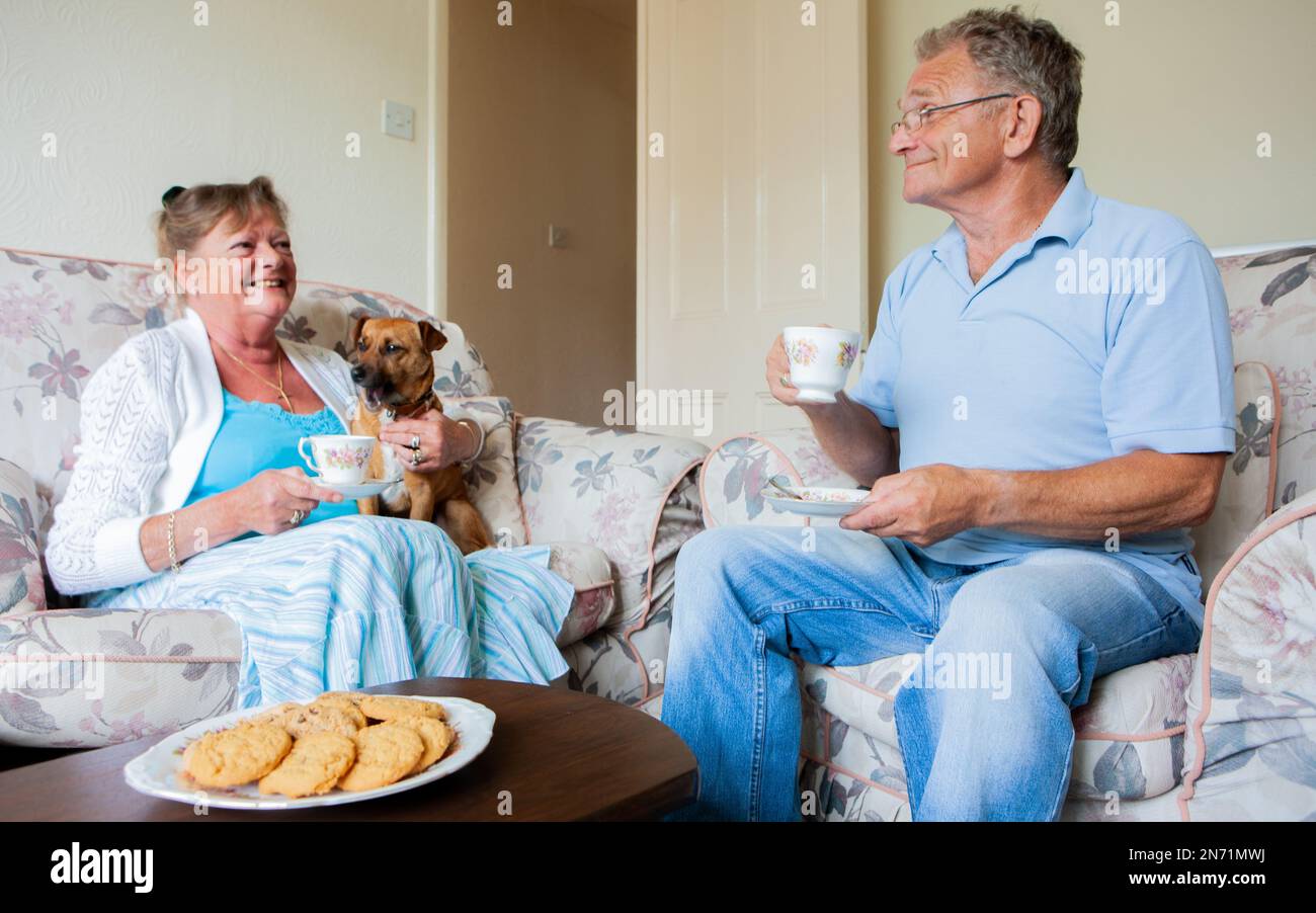 Ruhestand: Zeit für Tee. Ein älteres Paar und sein Hund entspannen sich zusammen mit Tee und Keksen, eine britische Tradition. Aus einer Reihe von zugehörigen Bildern. Stockfoto