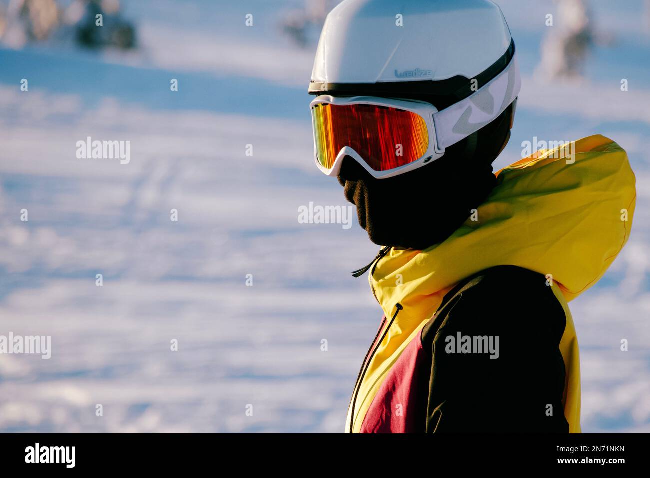 Ein junger Skifahrer in leuchtend gelber Jacke steht auf den Skiern und schaut in die Kameraobjektive. Stockfoto