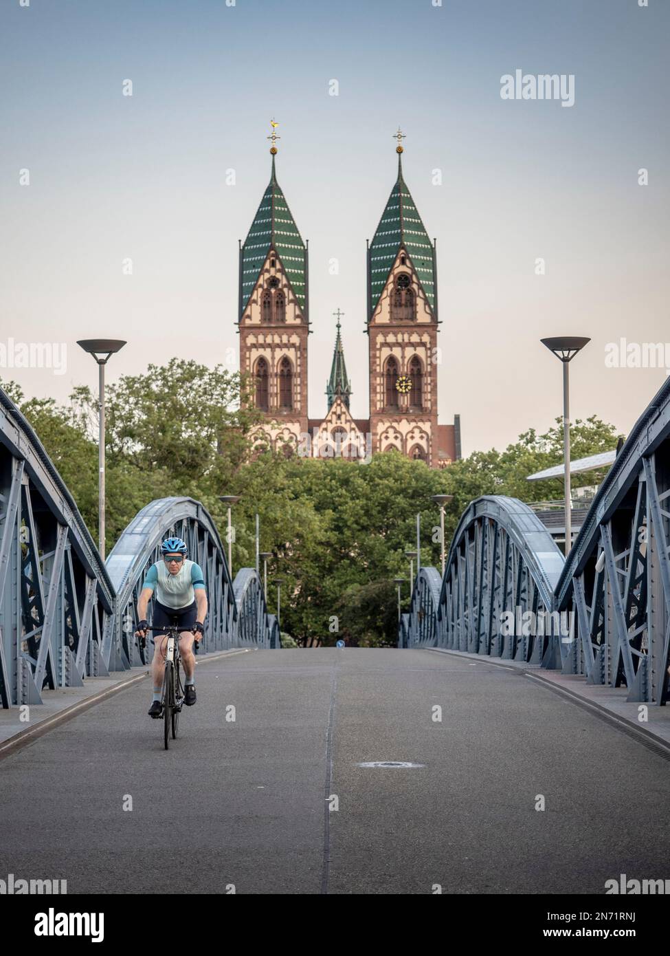Straßenradfahrer in Freiburg. Auf der "Blauen Brücke", die für den Autoverkehr gesperrt ist. Im Hintergrund befindet sich der Stühlinger Kirchplatz mit den beiden Kirchtürmen der Heiligen Herzkirche. Stockfoto