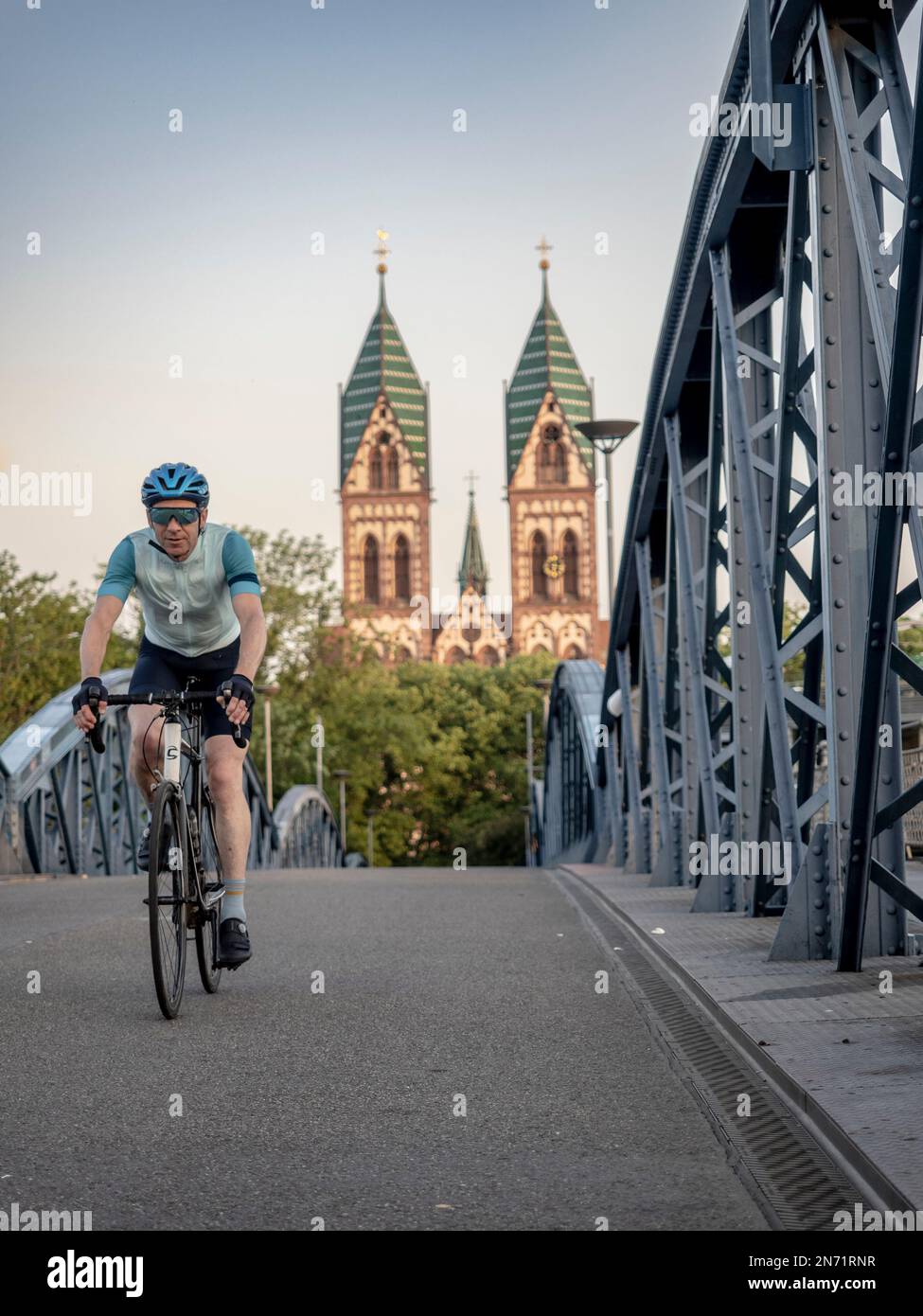 Straßenradfahrer in Freiburg. Auf der "Blauen Brücke", die für den Autoverkehr gesperrt ist. Im Hintergrund befindet sich der Stühlinger Kirchplatz mit den beiden Kirchtürmen der Heiligen Herzkirche. Stockfoto