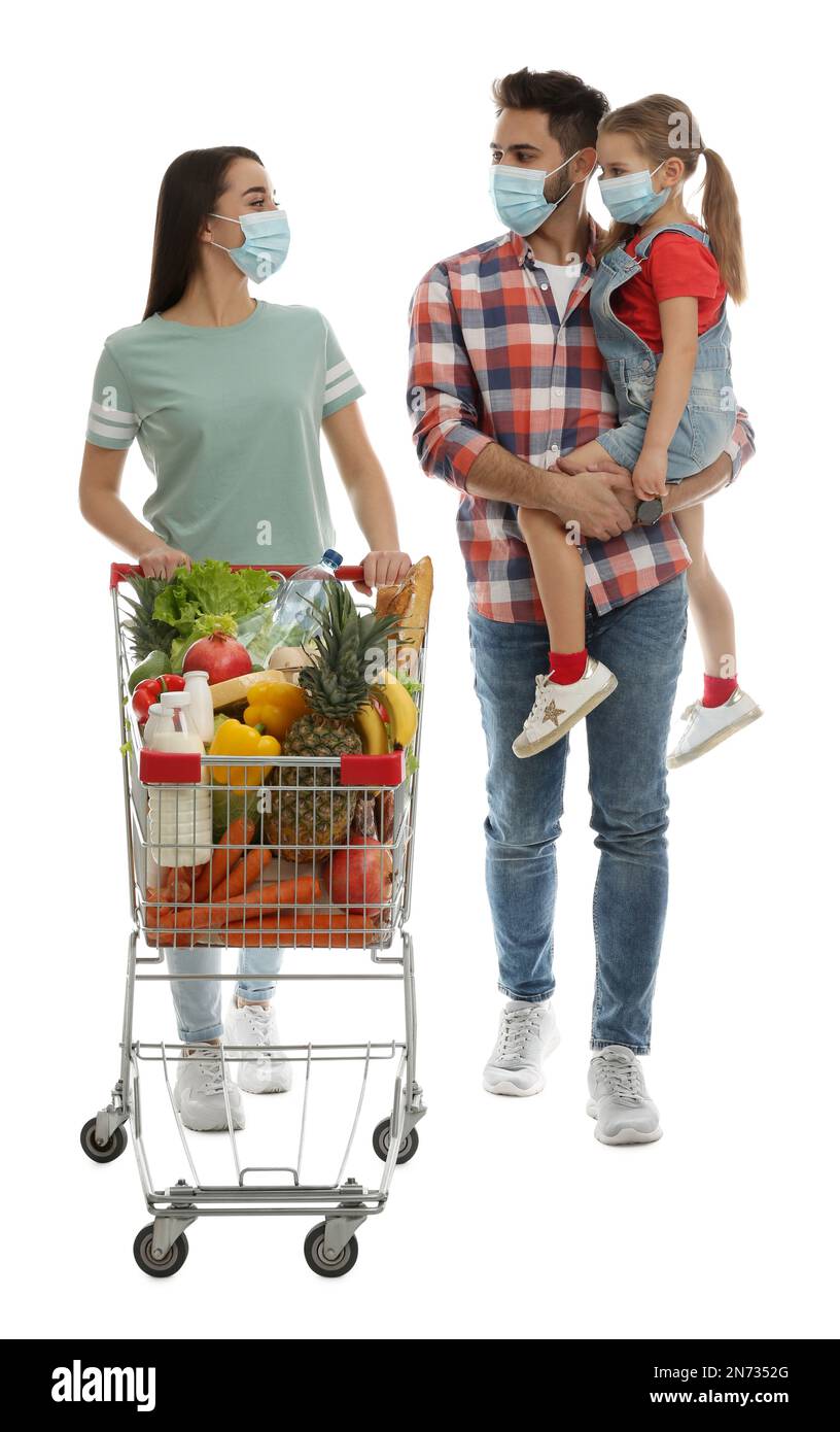 Familie in medizinischen Masken mit Einkaufswagen voller Lebensmittel auf weißem Hintergrund Stockfoto