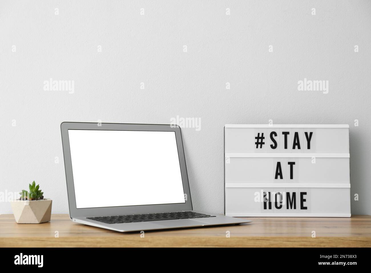 Laptop und Lightbox mit Hashtag BLEIBEN ZU HAUSE auf einem Holztisch. Botschaft zur Förderung der Selbstisolierung während der COVID-19-Pandemie Stockfoto