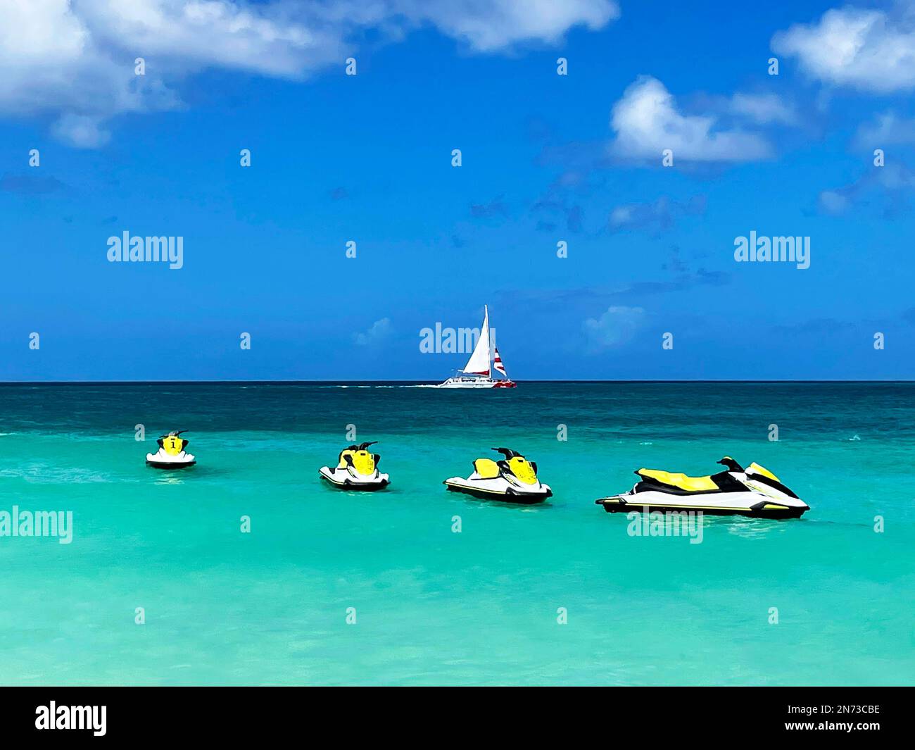 Wasserfahrzeuge, die vor der Küste von Aruba auf dem Karibischen Meer stehen. Ein Segelboot im Hintergrund. Stockfoto