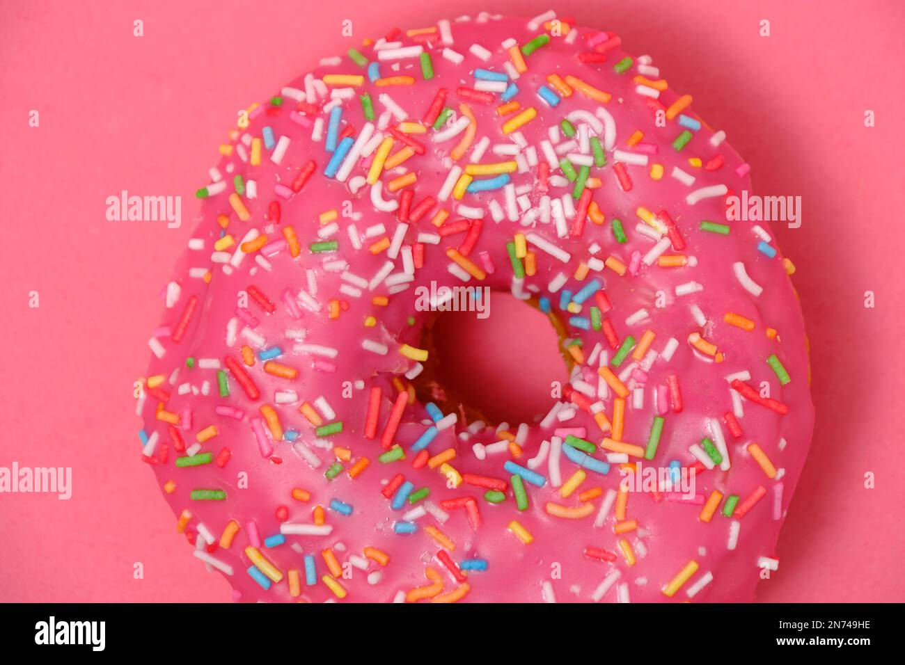 Donut mit pinkfarbenem Glasur und bunten Zuckerstreuseln. Auf pinkfarbenem Hintergrund Stockfoto