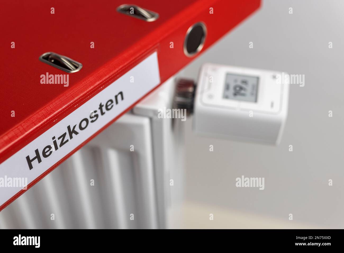 Roter Ordner mit Heizkosten für Etiketten, WLAN-Heizkörperthermostat FRITZ! DECT 302, Display zeigt 1ö °C an, Detail, Smart-Home-Technologie, Symbolbild, Netzwerke, digital, Energiekosten, steigende Heizkosten, weißer Hintergrund, Stockfoto