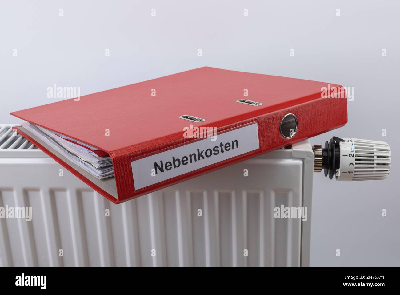 Roter Aktenordner mit den Wartungskosten für Etiketten liegt auf Heizkörper, Symbolbild, Heizrechnung, Energiekosten, steigenden Heizkosten, Weißer Hintergrund, Stockfoto