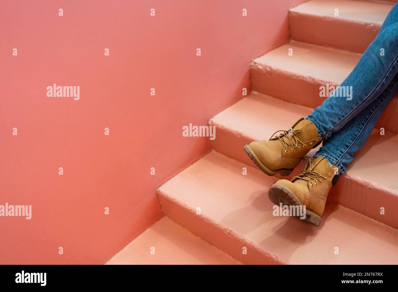 Beine in blauen Jeans braune Stiefel auf rosa Treppen. Werbetexte. Entspanntes Farbkonzept. Stockfoto