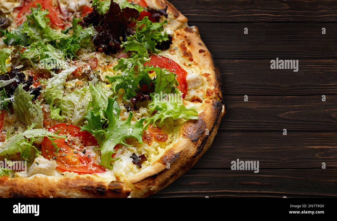 Gebackene Pizza mit Hühnchen, Tomaten, Salat und Käse, auf einem Holzbrett Stockfoto