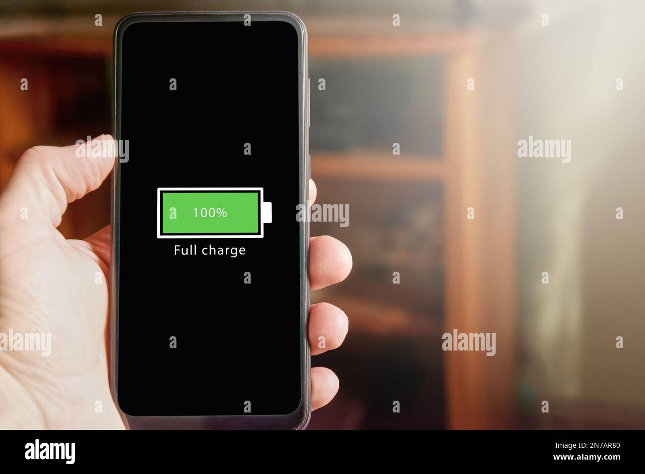 Nahaufnahme eines männlichen Smartphones mit einem Symbol für vollen Akku auf dem Bildschirm, das anzeigt, dass der Akkustand bei 100 % liegt. Voll aufgeladen Ba Stockfoto