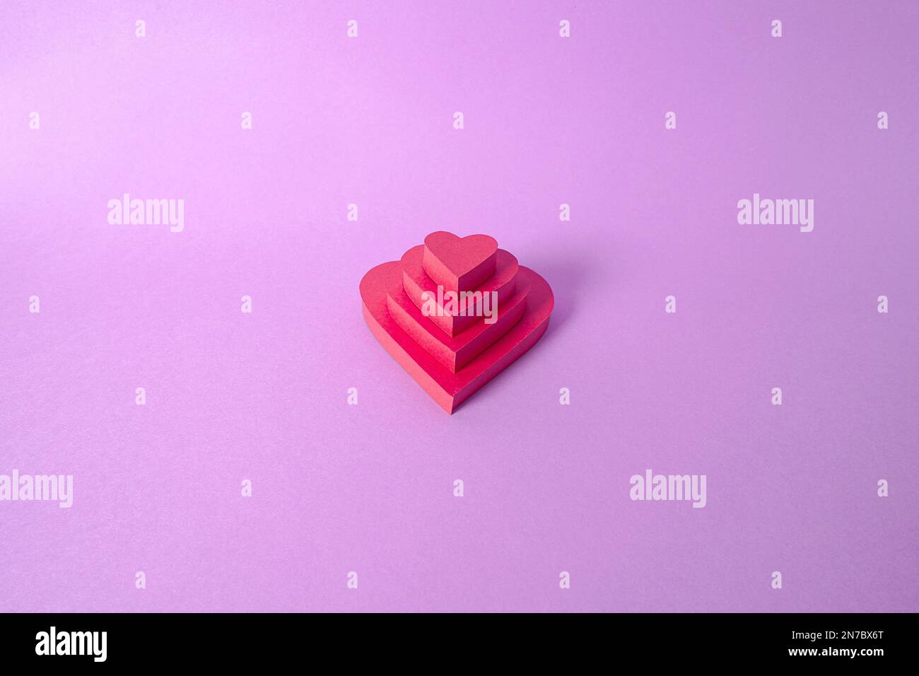 Mit Papier ausgeschnittene rote Herzen auf einem schönen lavendelfarbenen Hintergrund, gefertigt von Leidenschaft und Liebe für St. Valentinstag, Hochzeiten, Jubiläum oder Muttertag Stockfoto
