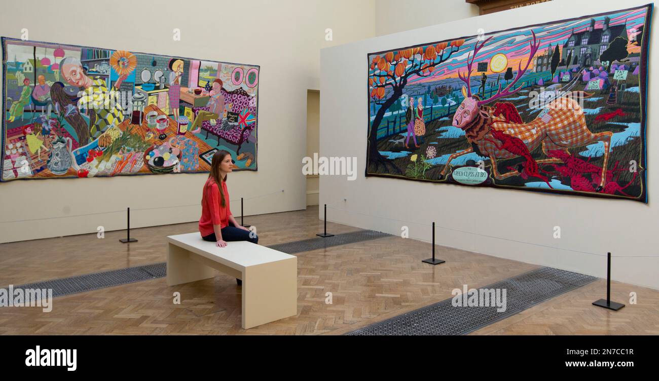A member of the Royal Academy staff poses for photographers during a media preview in front of woven tapestry works by British artist Grayson Perry, part of a series of works entitled 'The Vanity of Small Differences', which form part of the Royal Academy Summer show at the academy's galleries in London, Wednesday, June, 5, 2013. The summer show opens to the public from June 10 to Aug 18. (AP Photo/Alastair Grant) Stockfoto