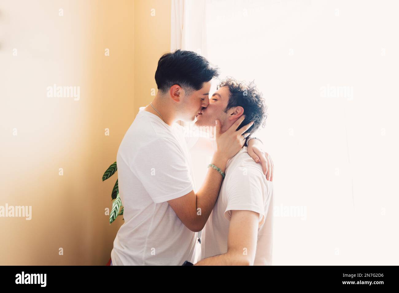 Zwei schwule Männer, die weiße T-Shirts tragen und sich romantisch auf den Mund küssen. LGBT-Beziehung Stockfoto