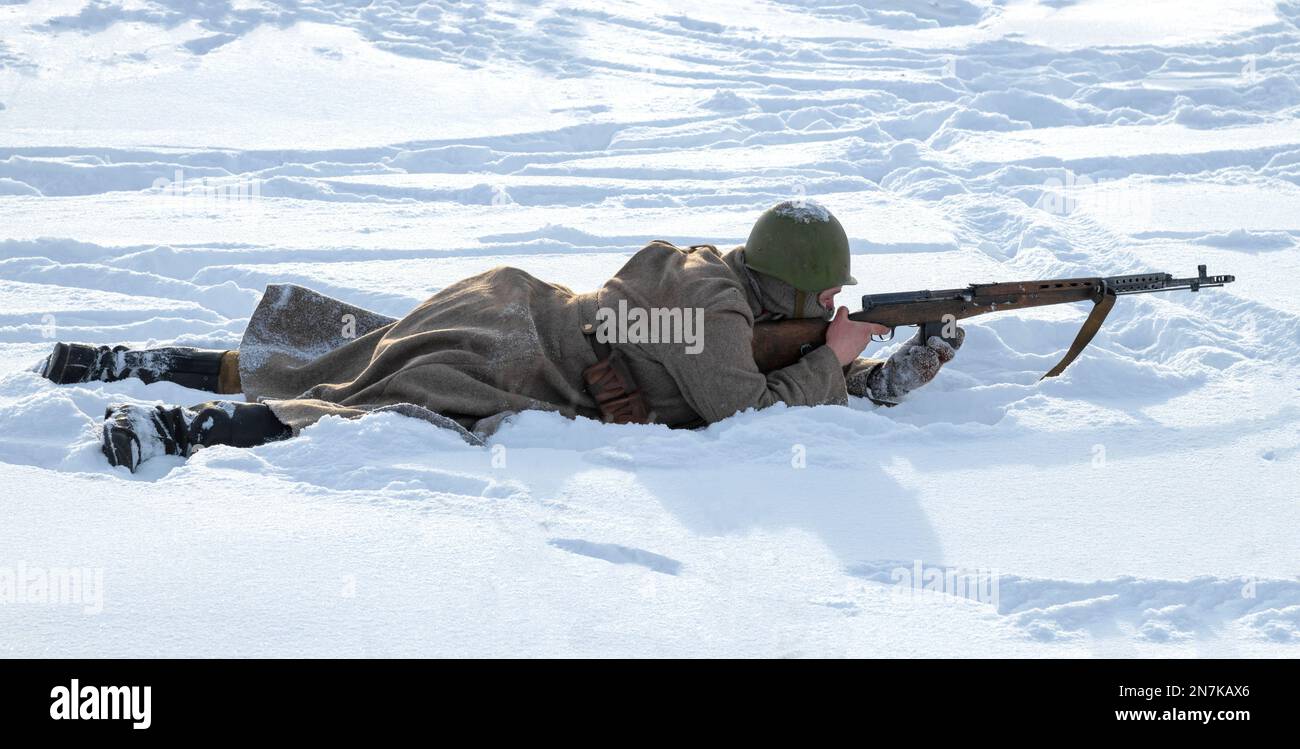 KRASNOE SELO, RUSSLAND - 05. FEBRUAR 2023: Der sowjetische Soldat liegt im Schnee und zielt mit einem SVT-40-Selbstladegewehr von Tokarev. Militärisch-historische Aufklärung Stockfoto