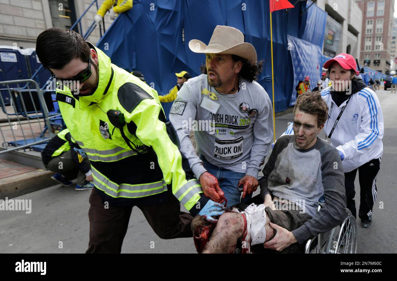 FILE - An emergency responder and volunteers, including Carlos Arredondo, in the cowboy hat, push Jeff Bauman in a wheelchair after he was injured in one of two explosions near the finish line of the Boston Marathon on April 15, 2013. (AP Photo/Charles Krupa, File) Stockfoto