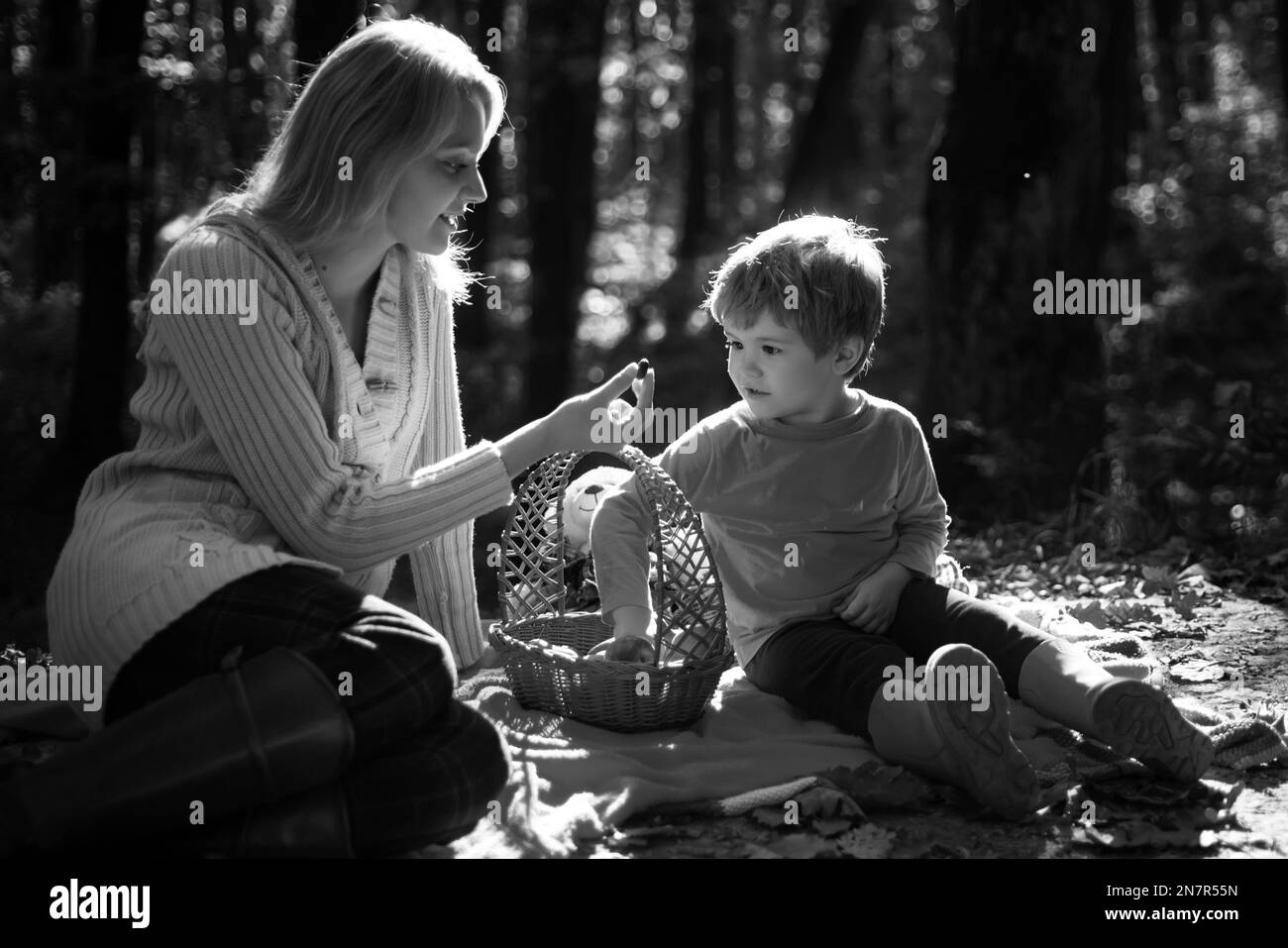 Junge Mutter, die ihrem kleinen Sohn beim Herbstpicknick eine süße Saisonberrie gibt. Mama und Kind sitzen auf der Picknickdecke und essen aus dem Picknickkorb Stockfoto