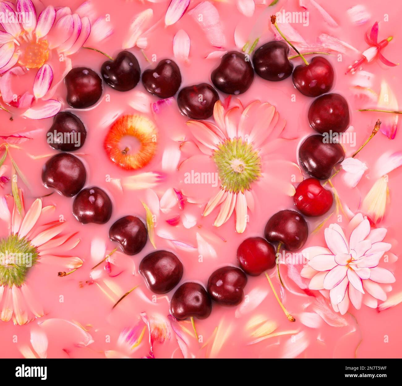 Herzförmiges süßes Kirschmuster und Blumen auf Rosenwasser, flach liegend Stockfoto