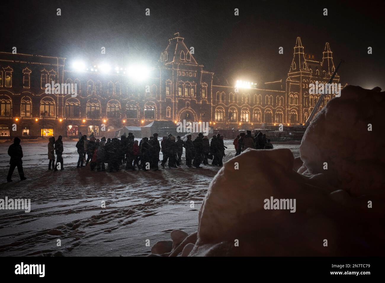 People walk through a snow covered Red Square during a snowfall in Moscow, Russia, Monday, March 25, 2013, with the illuminated GUM, State shopping mall in the background. A heavy snowfall has continued for the second day in Moscow with temperatures hovering around -9 degrees Celsius (17 F). (AP Photo/Alexander Zemlianichenko) Stockfoto