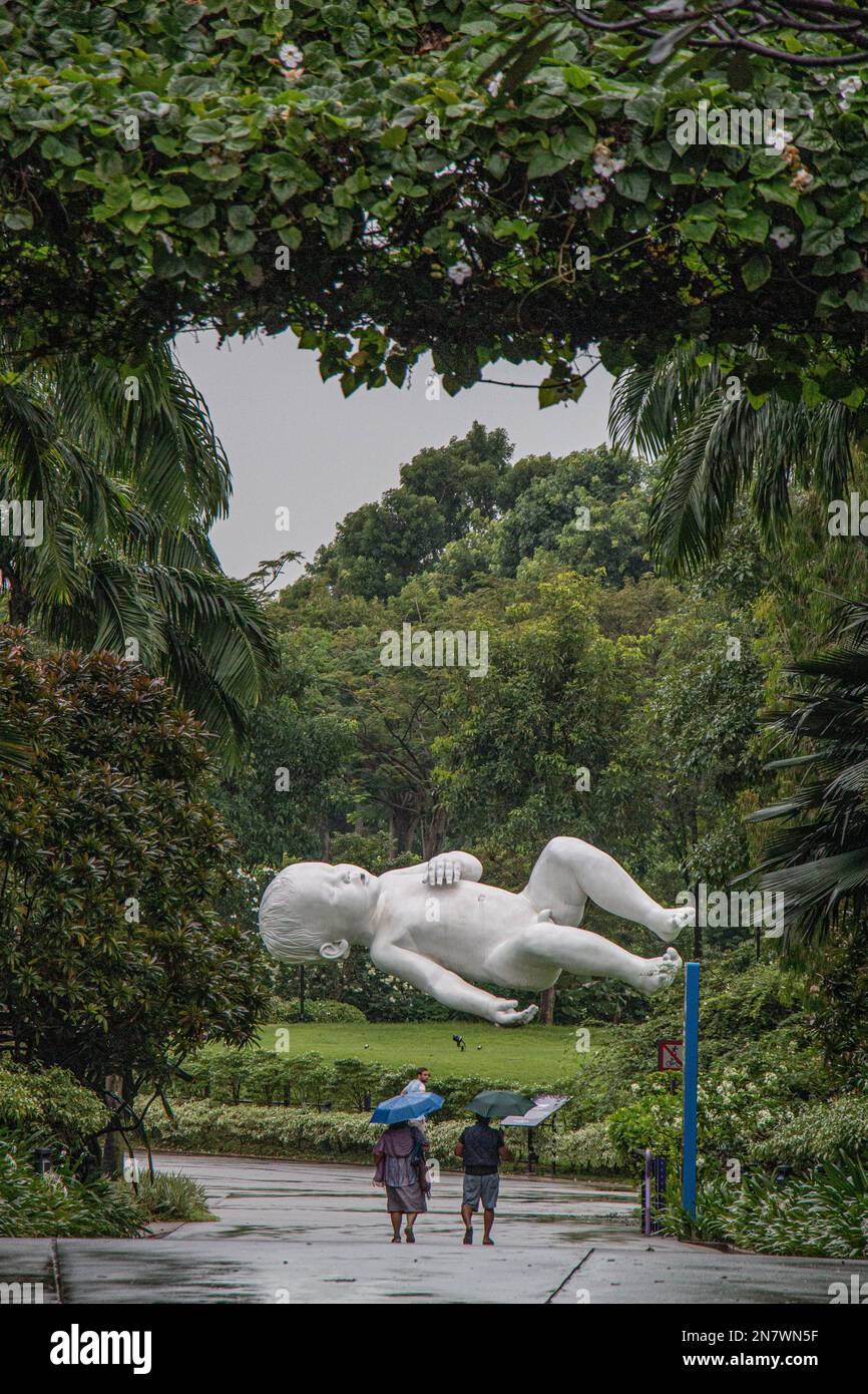 Regnerischer Tag in den Gärten an der Bucht, Singapur, mit zwei Personen, die zu Fuß unterwegs sind, und der Skulptur eines schlafenden Kindes, das in der Luft schwimmendes Baby namens Planet Stockfoto