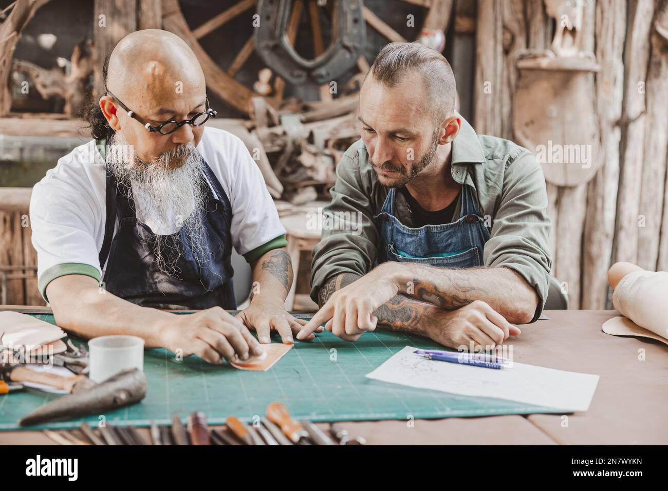 Meister des Lederpersonals, unterrichtet und trainiert jungen Mann für die Herstellung handgefertigter Ledertaschen Stockfoto
