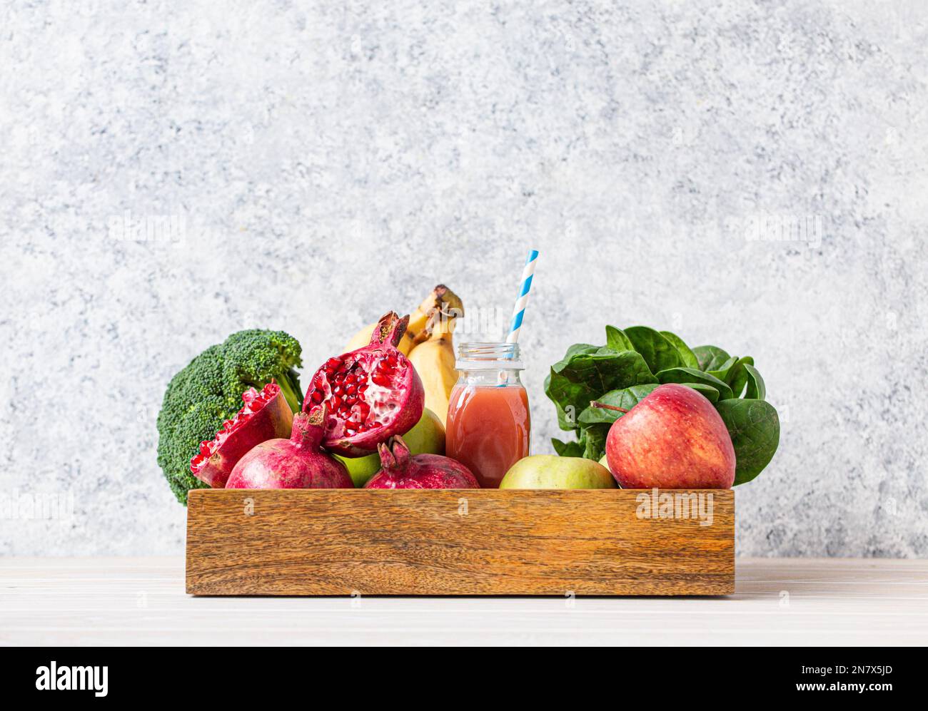 Obst, Gemüse, Gemüse in einer Holzschale und frischer Smoothie oder Saft in der Flasche mit Papierstroh auf dem Tisch nahe der weißen Wand, Entgiftung, Diät, sauberes Essen Stockfoto