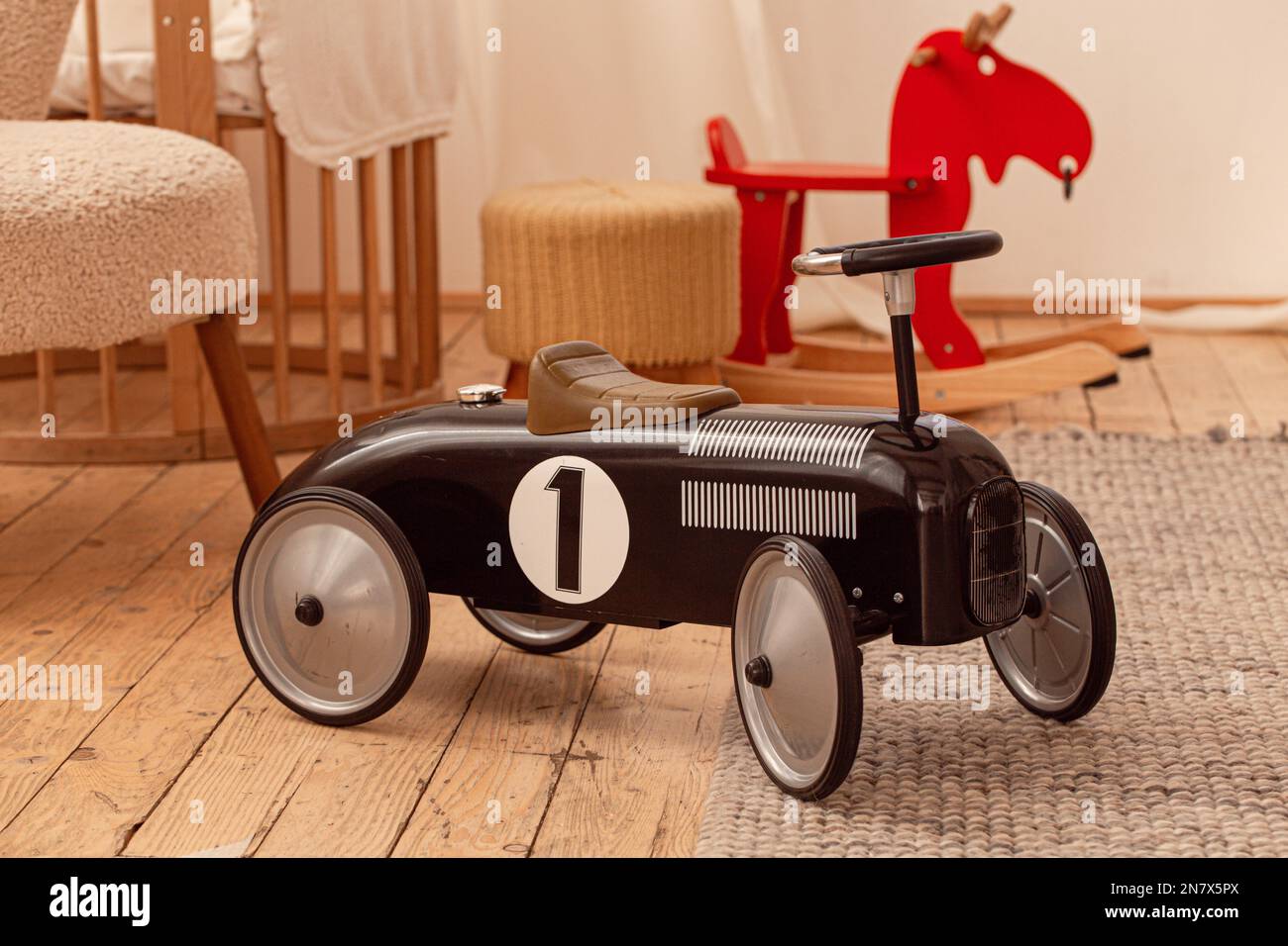 Schwarzes Retro-Rennauto im skandinavischen Kinderzimmer mit Spielzeug, Bett, Laufstall, Stuhl und Schaukelpferd aus Holz. Stockfoto