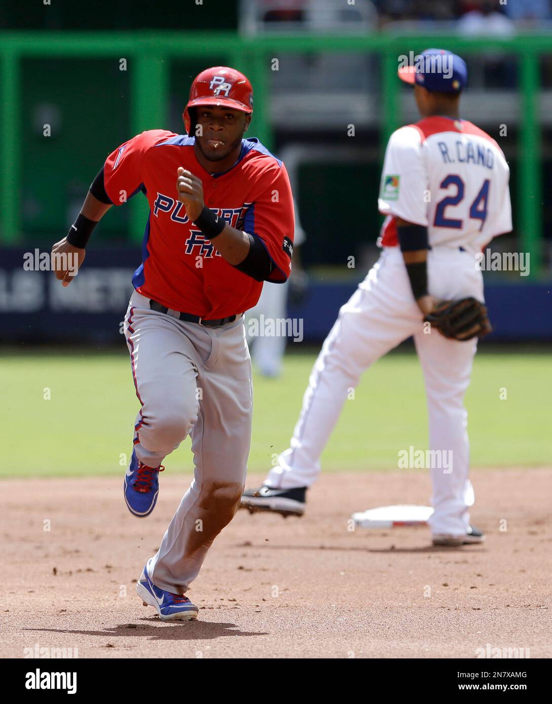 Puerto Rico's Irving Falu, left, heads to third base after advancing to second base on a throwing error by Dominican Republic catcher Carlos Santana, as second baseman Robinson Cano (24) awaits the throw during the third inning of a second-round game of the World Baseball Classic in Miami, Saturday, March 16, 2013. The Dominican Republic won 2-0. (AP Photo/Alan Diaz) Stockfoto