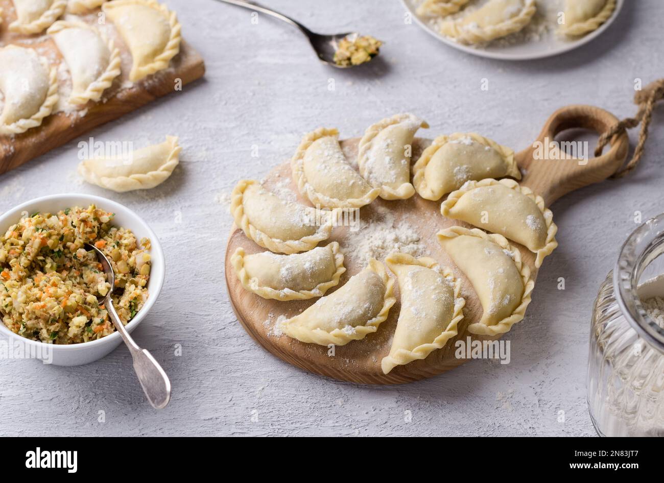 Hausgemachte rohe gefrorene vegane Knödel, Vareniki, Pierogi, Kreplach gefüllt mit veganem Linsenfleisch, Karotten, Zwiebeln, Kräutern und Gewürzen auf Holzbrett Stockfoto