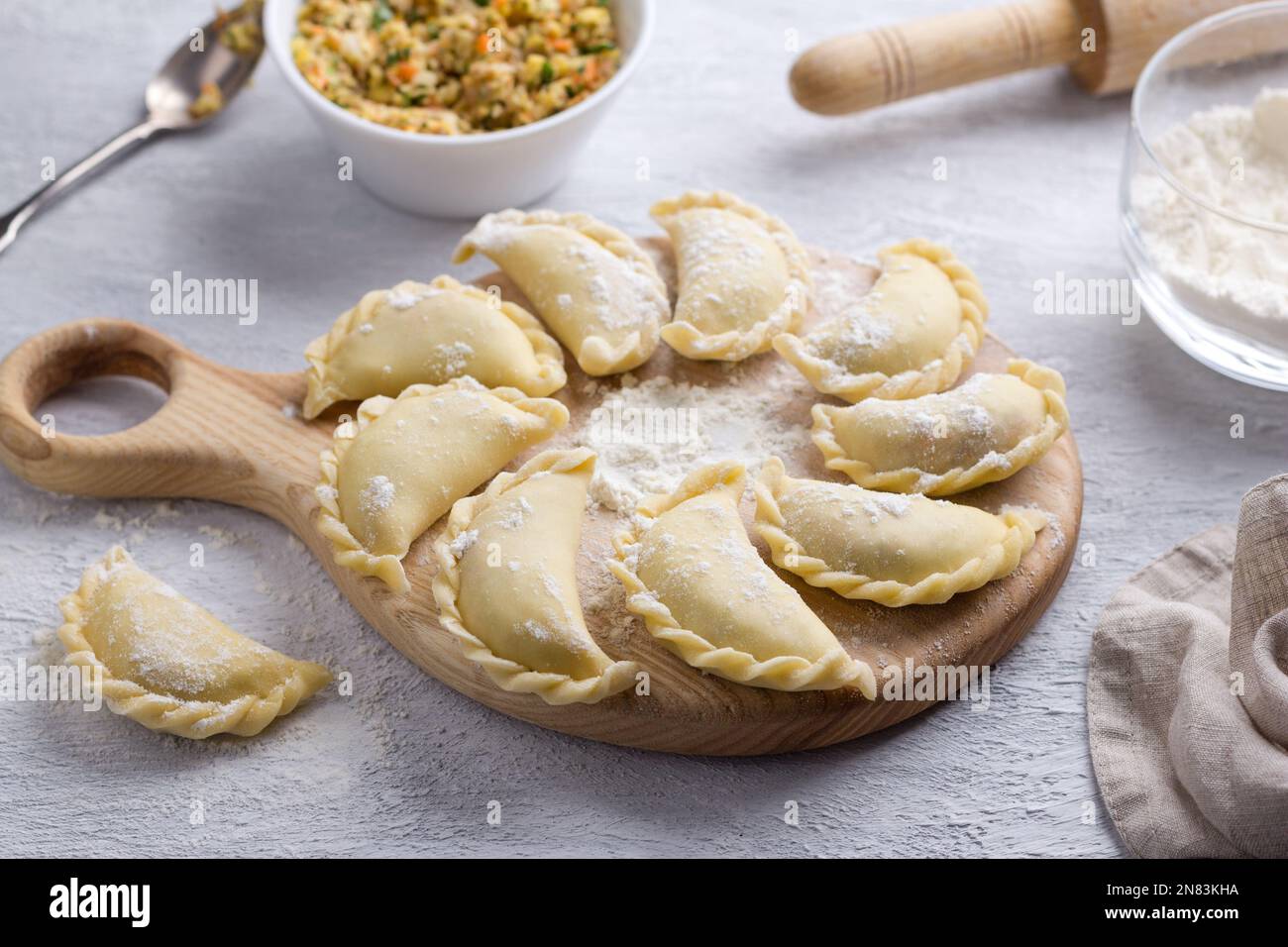Hausgemachte rohe gefrorene vegane Knödel, Vareniki, Pierogi, Kreplach gefüllt mit veganem Linsenfleisch, Karotten, Zwiebeln, Kräutern und Gewürzen auf Holzbrett Stockfoto