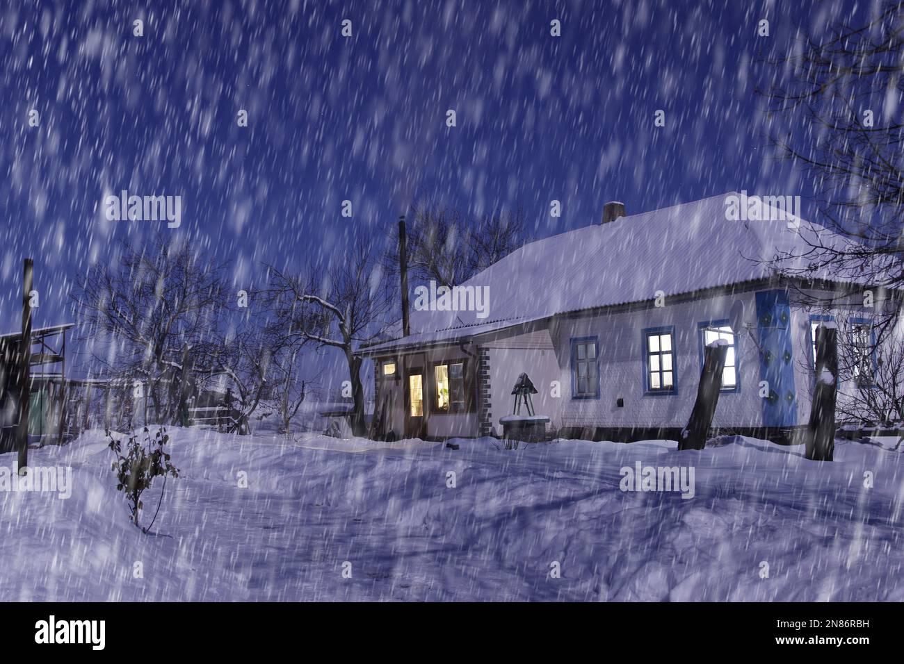 Wunderschöner Blick auf das schneebedeckte Haus bei Nacht bei starkem Schneefall. Alles ist mit Schnee bedeckt. Rauch kommt aus dem Kamin. Stockfoto