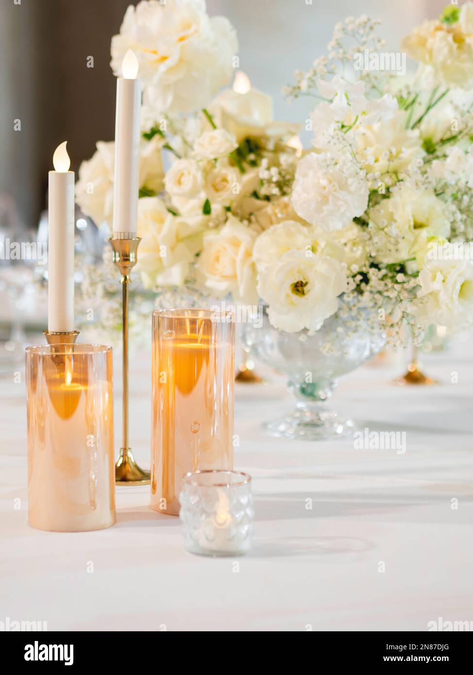 Tisch für Bankett serviert. Elektrische und echte Kerzen in glänzenden Kerzenhaltern als Dekoration. Tisch mit weißer Tischdecke und floraler Zusammensetzung. Ein Blumenstrauß Stockfoto