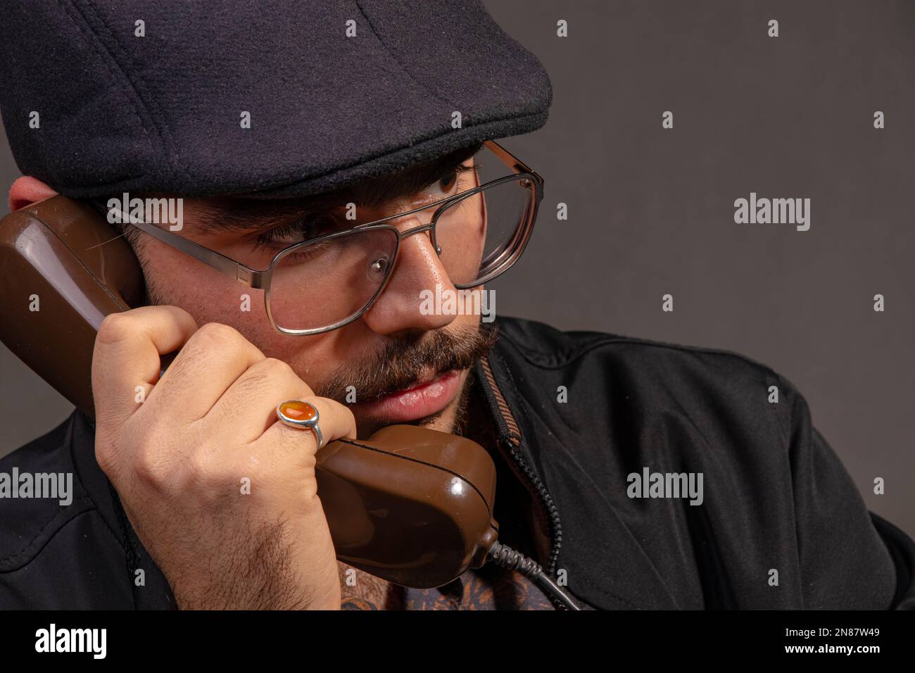 Ein ruhiger Mann mit Brille, braunem Hemd und schwarzer Jacke, der jemanden mit einem alten Telefon anruft Stockfoto