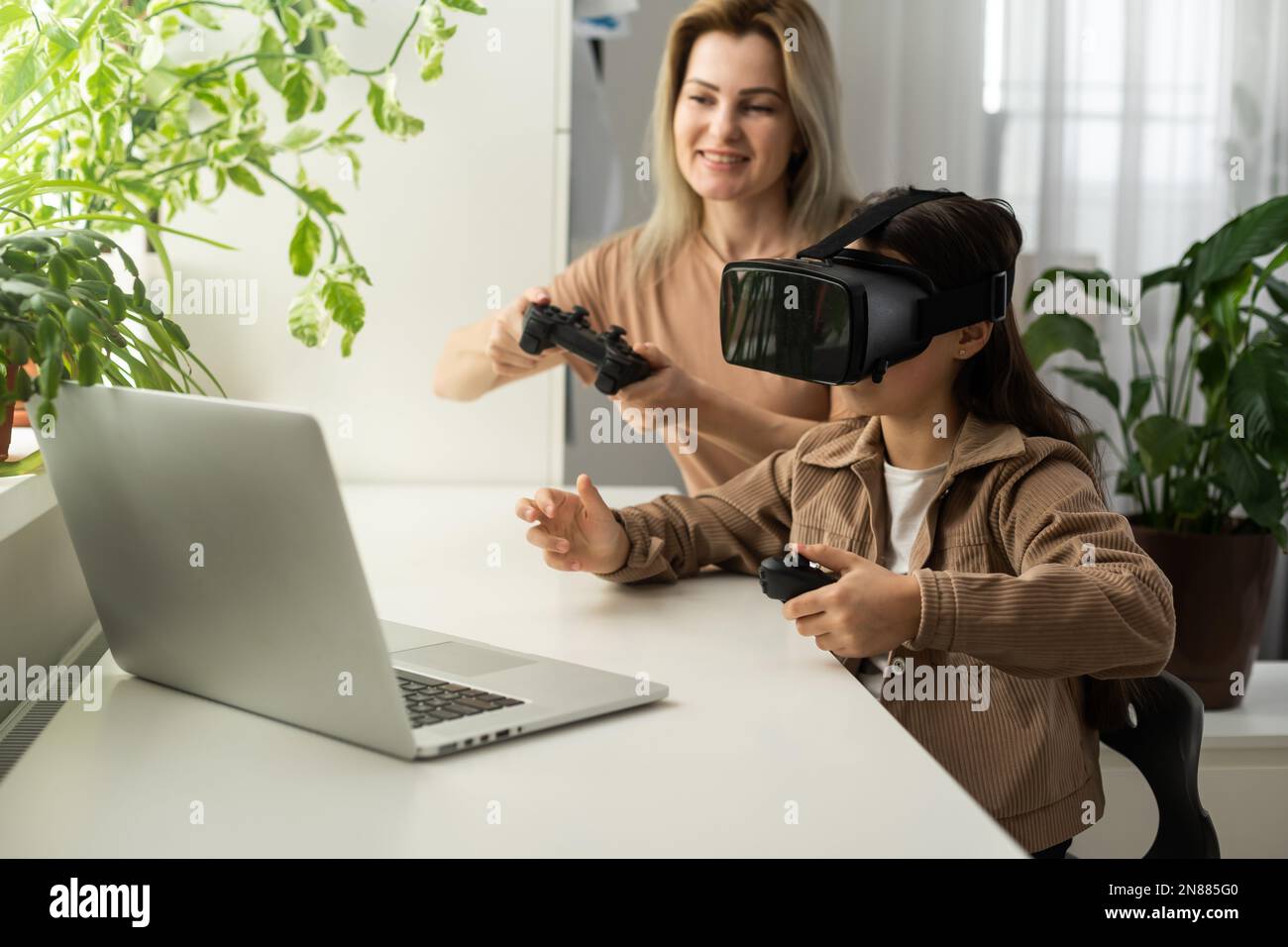 Familien und neue Technologien. Lächelnde Arbeit-zu-Hause-Mutter, die mit ihrer Tochter einen VR-Helm trägt und die virtuelle Realität erforscht. Neugieriges Teenager-Mädchen Stockfoto