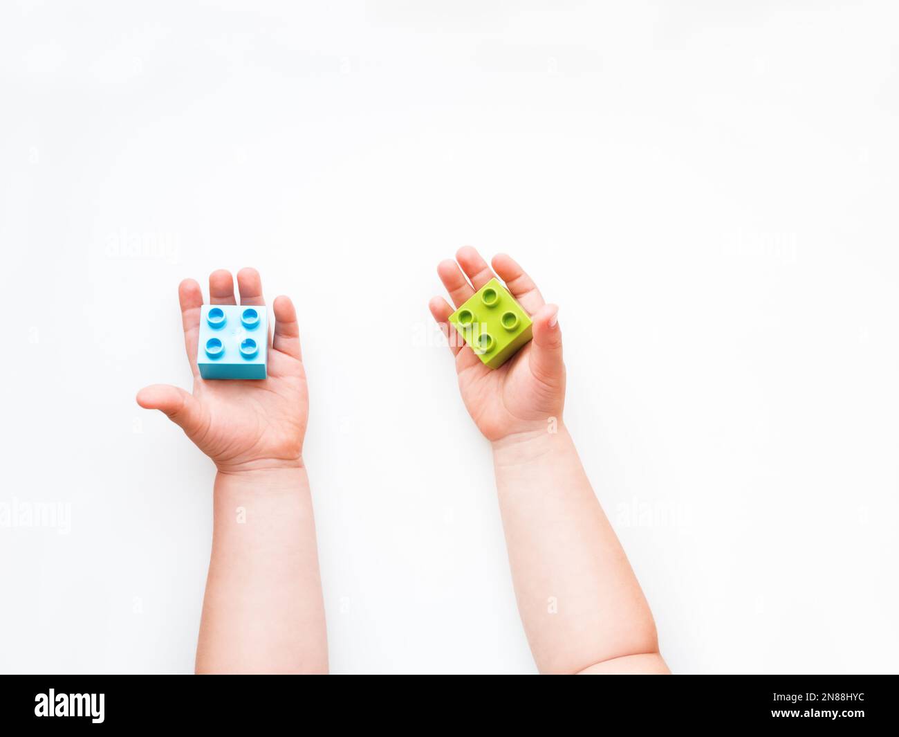 Das Kind hat grüne und blaue Bausteine in der Faust. Kinderhände mit Ziegelspielzeug auf weißem Hintergrund. Pädagogisches Spielzeug, flach liegend, Draufsicht. Stockfoto