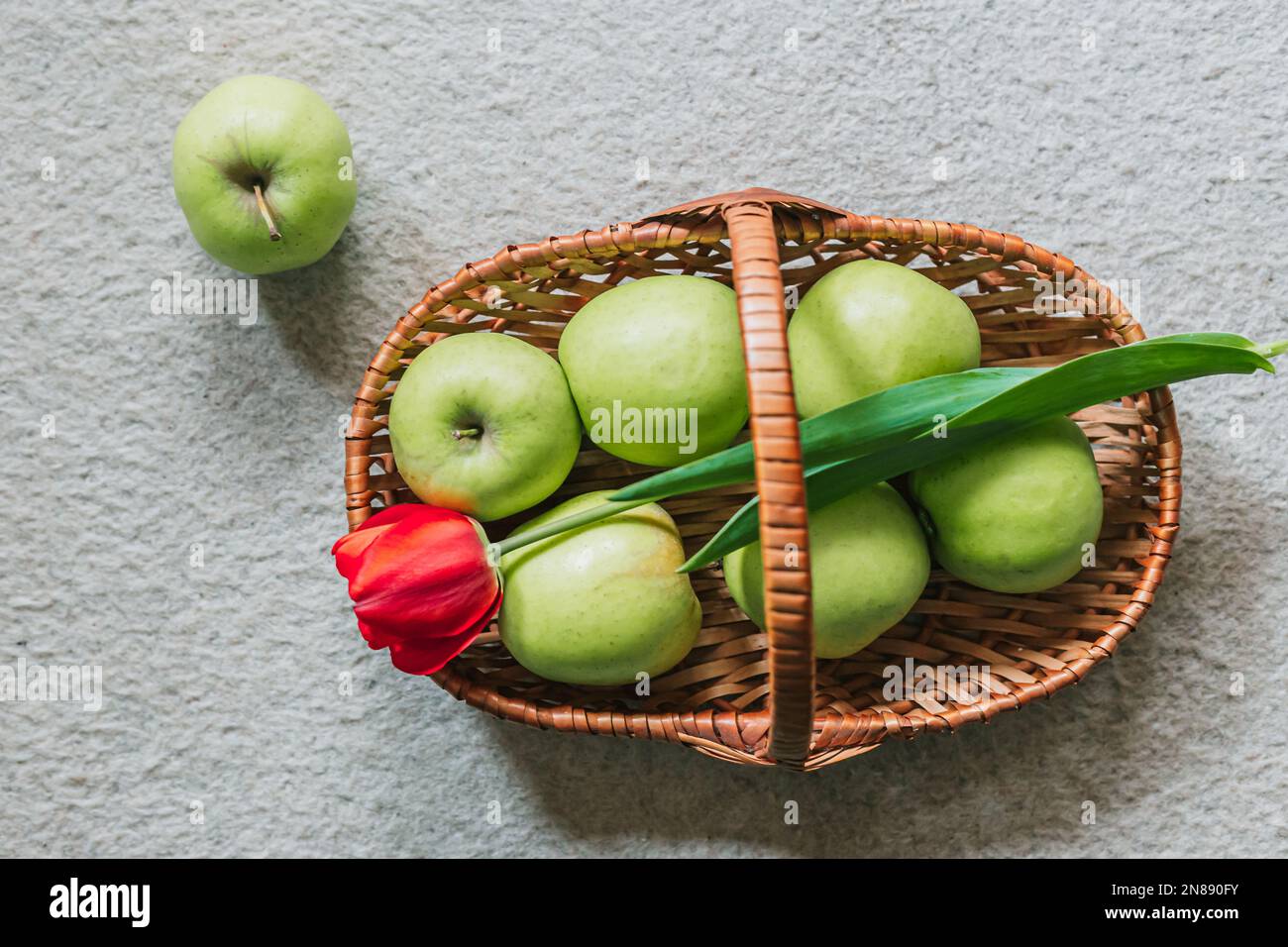 Frische, grüne Äpfel im Korb und eine rote Tulpe. Draufsicht, Frühjahrssymbolik. Speicherplatz kopieren Stockfoto