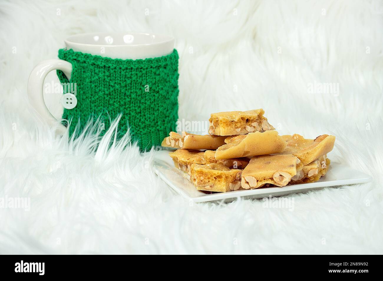 Weihnachtliche Erdnussbutter auf weißem Fell mit weißem Becher und grünem Strickwärmer Stockfoto