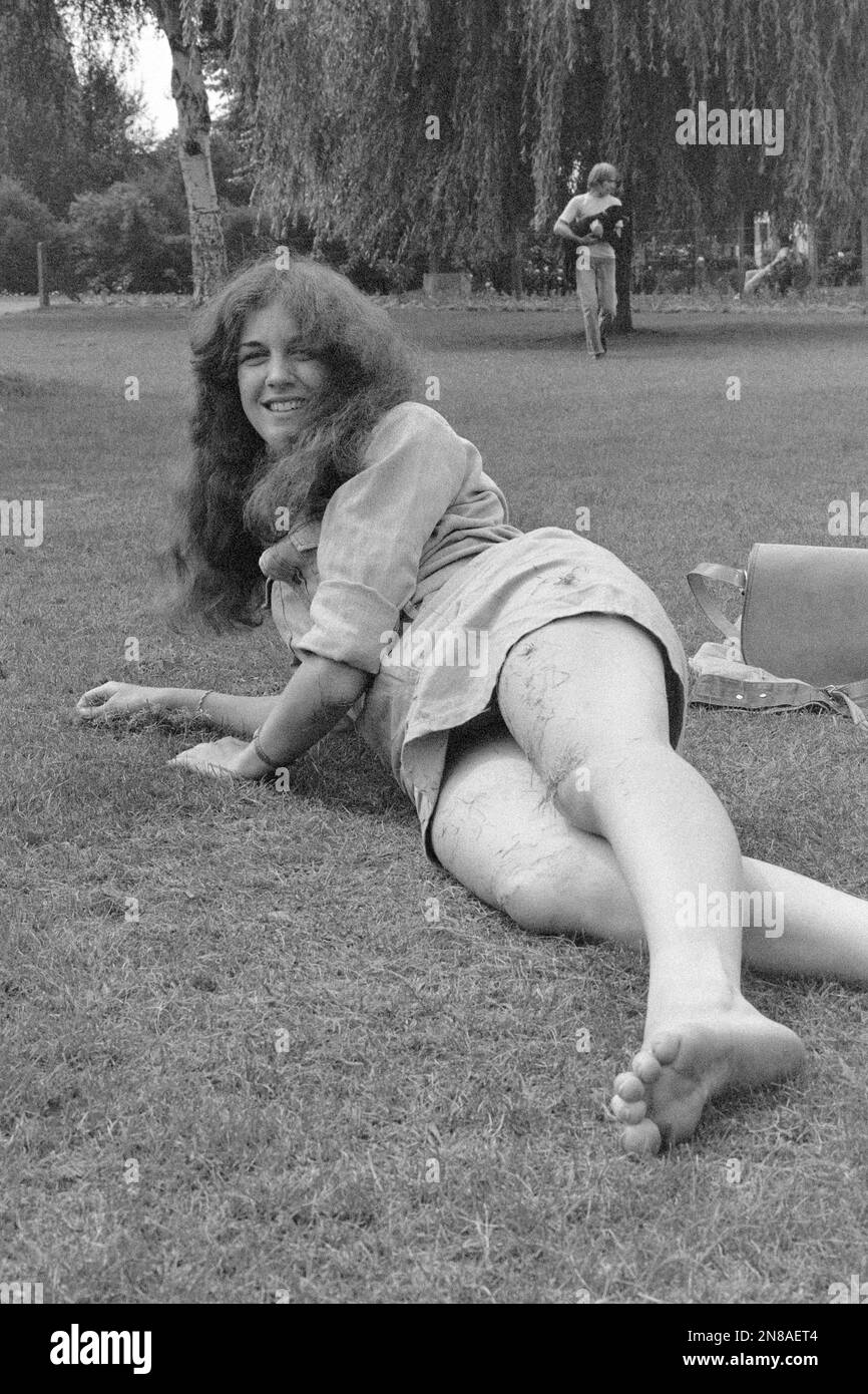 Junge Frau, die im öffentlichen Park auf dem frisch geschnittenen Gras liegt und den entspannten warmen Sommertag 1980er england uk genießt Stockfoto