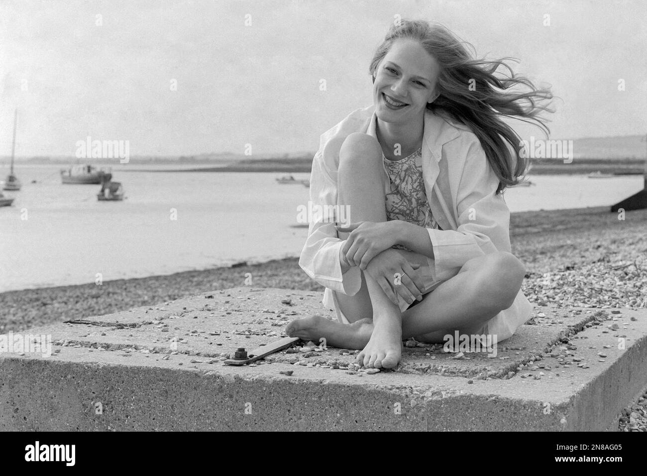 Junge, hübsche, blonde Frau, die am Meer sitzt und ein übergroßes Hemd gegenüber der Walinsel portsmouth england 1990er trägt Stockfoto