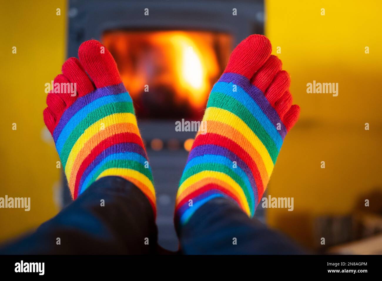 Wärmt die Füße, während sie farbenfrohe gestreifte Socken mit beleuchtetem Holzbrenner tragen, der im Hintergrund leuchtet Stockfoto
