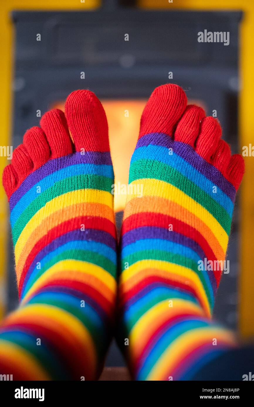 Wärmt die Füße, während sie farbenfrohe gestreifte Socken mit beleuchtetem Holzbrenner tragen, der im Hintergrund leuchtet Stockfoto