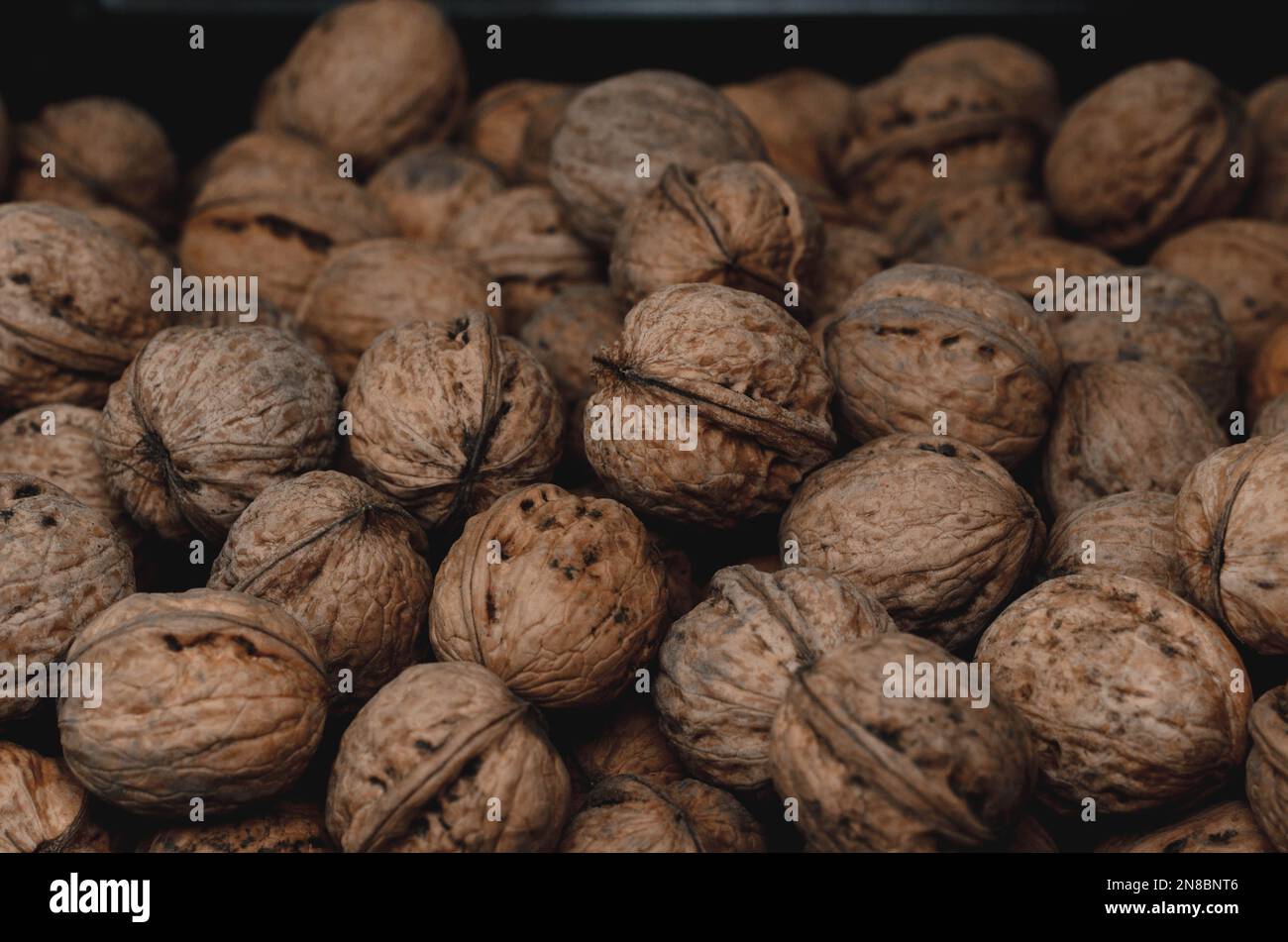 Walnuss-Hintergrund Nahaufnahme. Nicht ausgelöste, getrocknete Samen des Walnussbaums Juglans regia. Ein Haufen ganzer Nüsse mit Schalen, die als Snack zum Backen verwendet werden Stockfoto