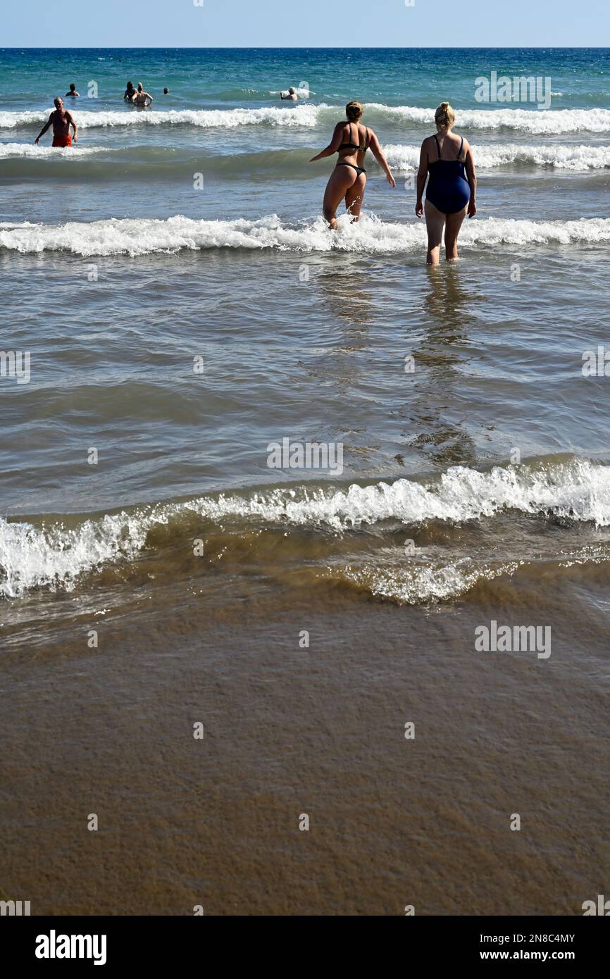 Menschen, die durch leichte Brandung am Sandstrand Playa del Inglés ins Meer gehen, mit anderen im Meer, Maspalomas Stockfoto