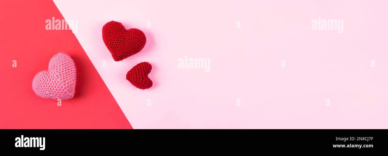 Drei gestrickte Herzen auf pinkfarbenem und rotem Hintergrund. Liebeskonzept. Banner, flach liegend. Stockfoto
