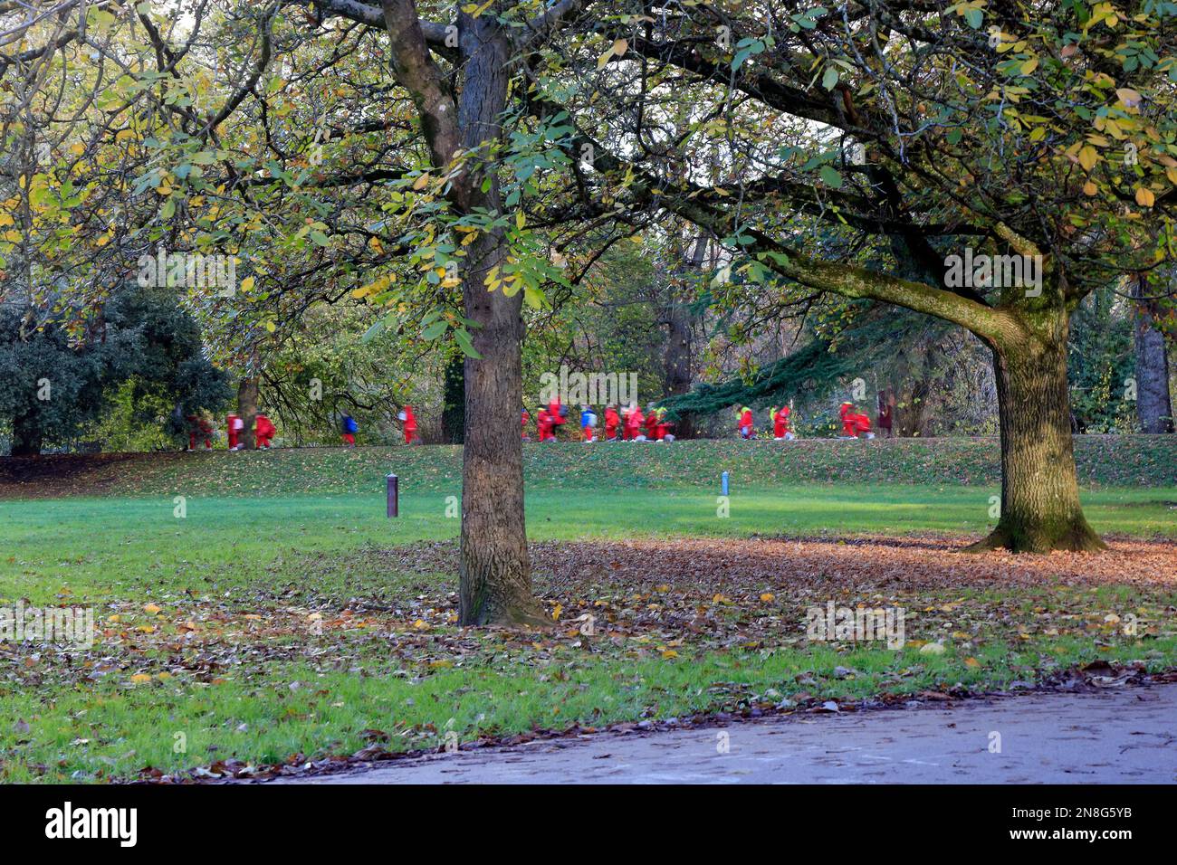 Kindergärtnerinnen in einer Reihe mit roter Kleidung folgen Lehrern durch den Park in Sophia Gardens, Cardiff, 2022. Verschwommene Kinder, unidentifizierbar. Stockfoto