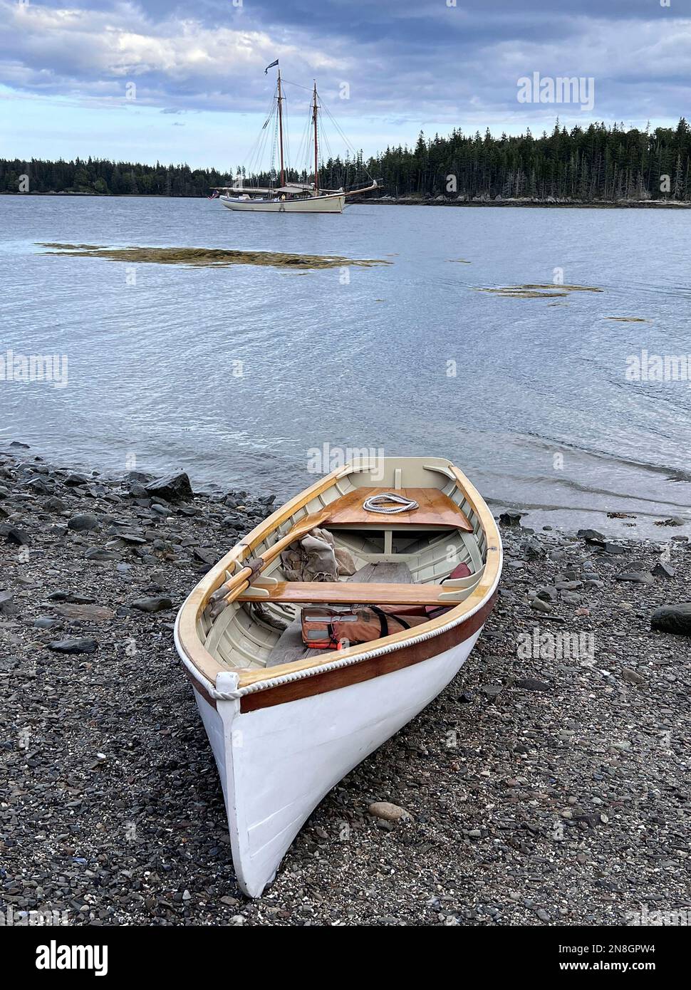 Ein altes Holzdinghy hielt an einer ruhigen Ankerstelle in Maines Penobscot Bay mit einem hohen Segelschiff im Hintergrund an. Stockfoto
