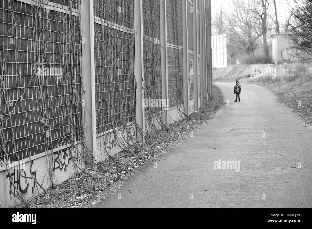 Eine Graustufenaufnahme eines Fußwegs neben einer Schallmauer mit einem stehenden Jungen in Posen, Polen Stockfoto