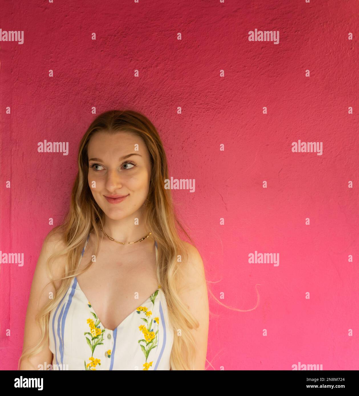 Ein blondes Mädchen, 20-35 Jahre alt, das an einer rosa Wand steht Stockfoto