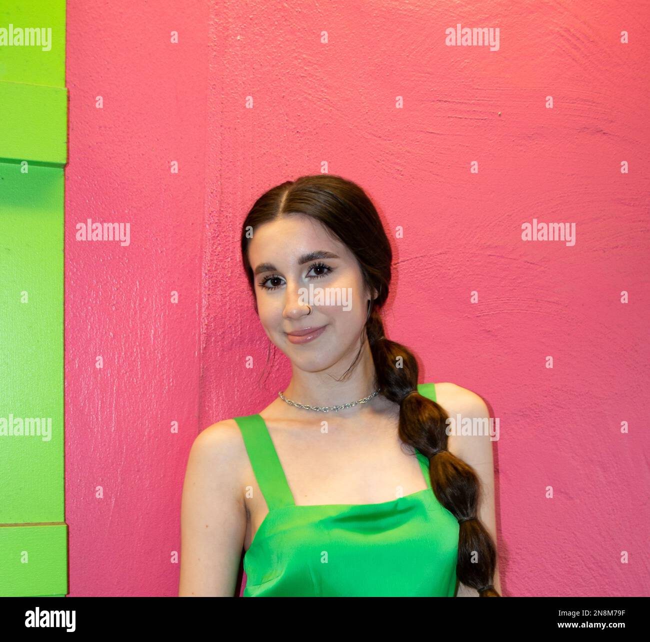 Ein 20-35-jähriges Mädchen, das ein grünes Kleid trägt und draußen an einer rosa Wand steht Stockfoto